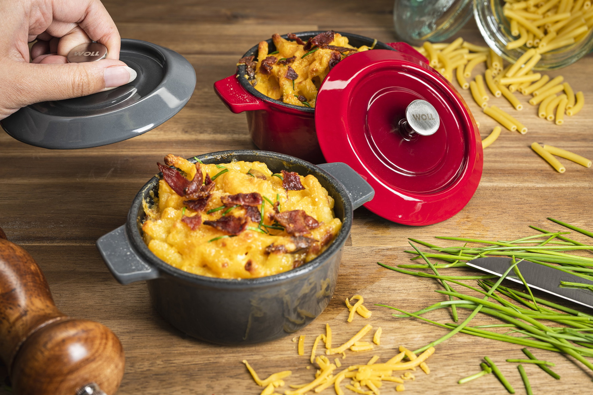 In zwei runden Mini-Kasserollen der Serie „Iron” wurden frische Mac & Cheese zubereitet. Die Deckel wurden hochgenommen und an die Kasserollen angelehnt. Außen herum liegen Nudeln, Käse und Kräuter.