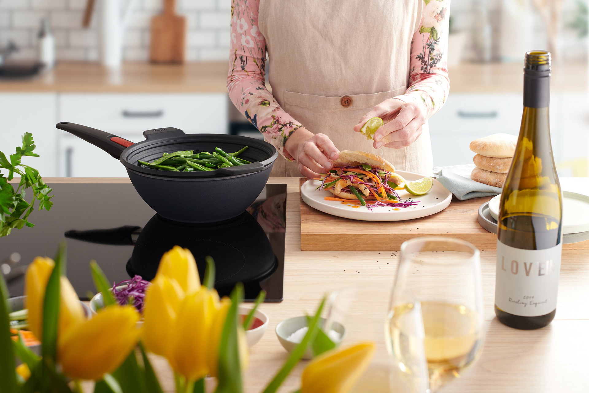 In einer runden Diamond Lite Wok- und Rührpfanne wird Gemüse in einem Silikoneinsatz gedämpft. Auf dem Teller liegt ein gefülltes Fladenbrot.