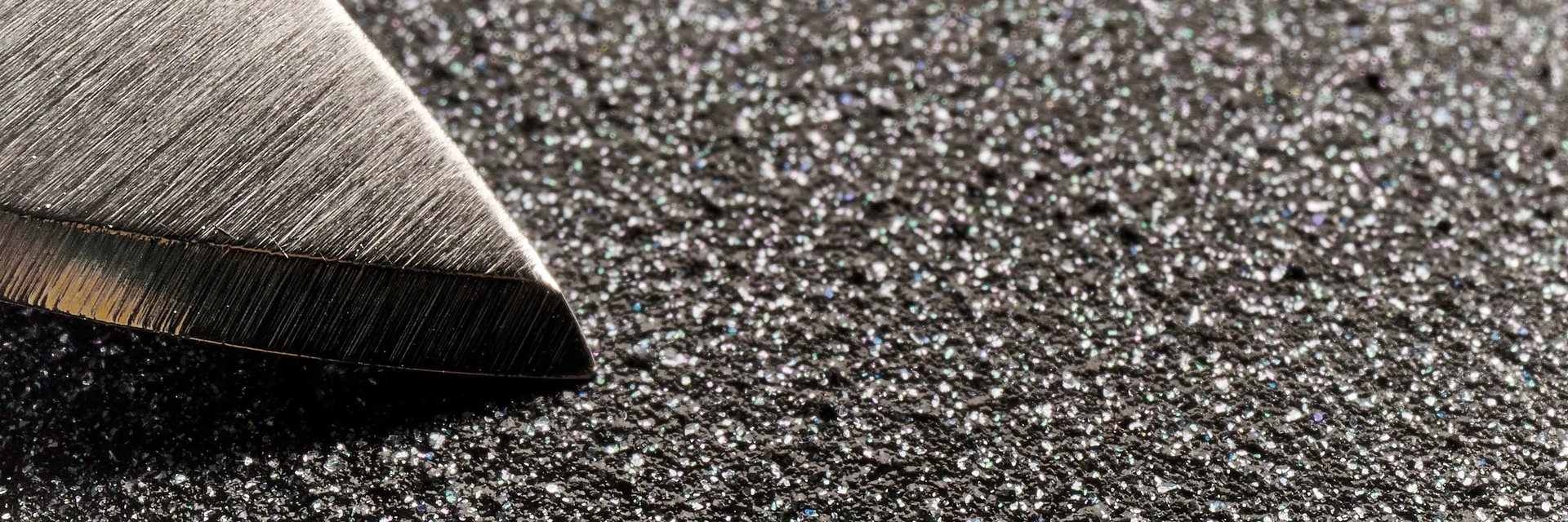 In der Makroaufnahme ist die Oberflächenstruktur einer PFAS-freien Beschichtung im Vergleich zu einer glatten Messerspitze zu erkennen.