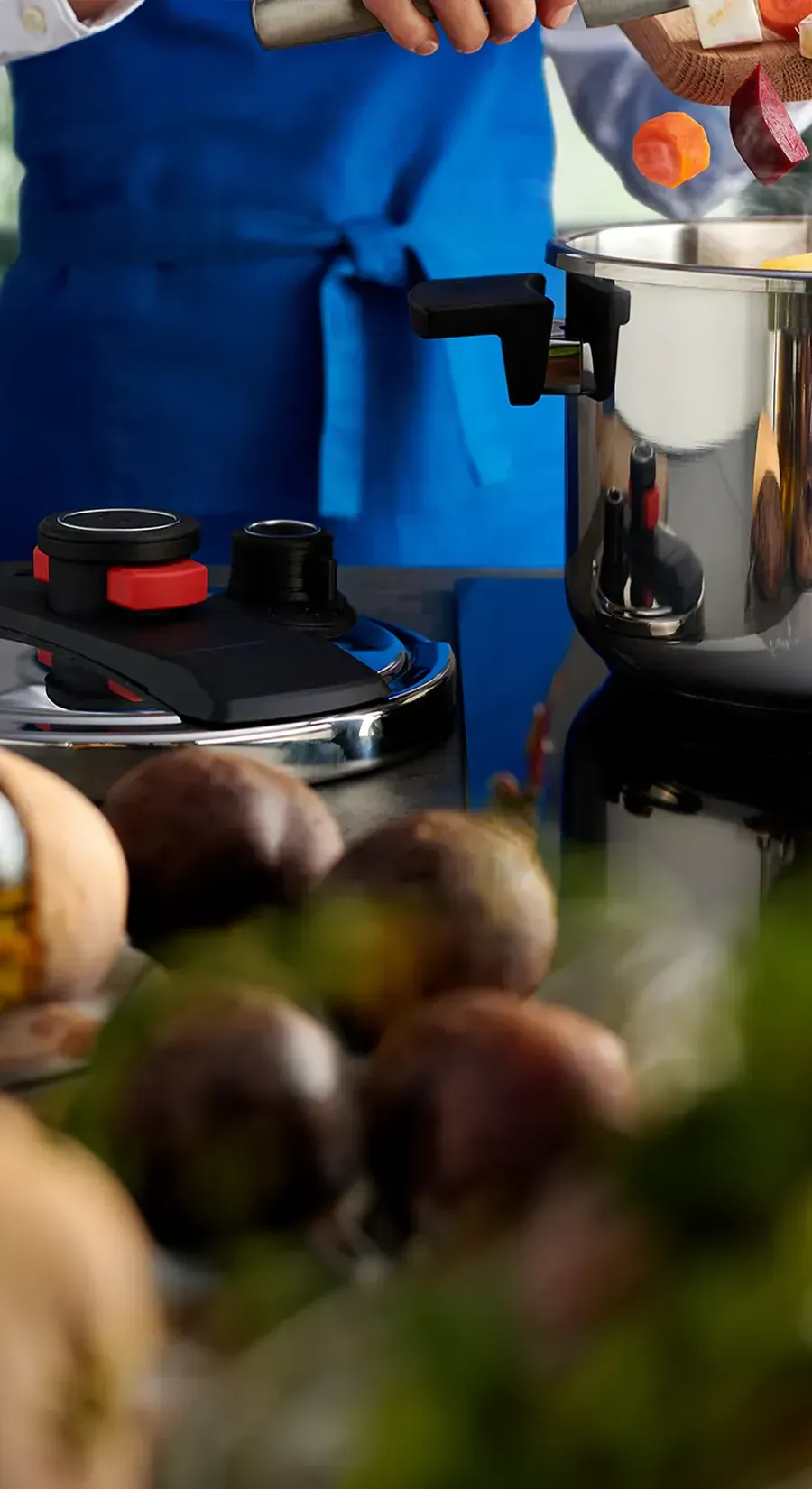 Auf dem Herd steht ein dampfender Pressure-Pro-Topf, während das frisch geschnittene Gemüse mit dem Messer vom Brett in den Topf gegeben wird. Der Deckel liegt links auf der Arbeitsplatte.