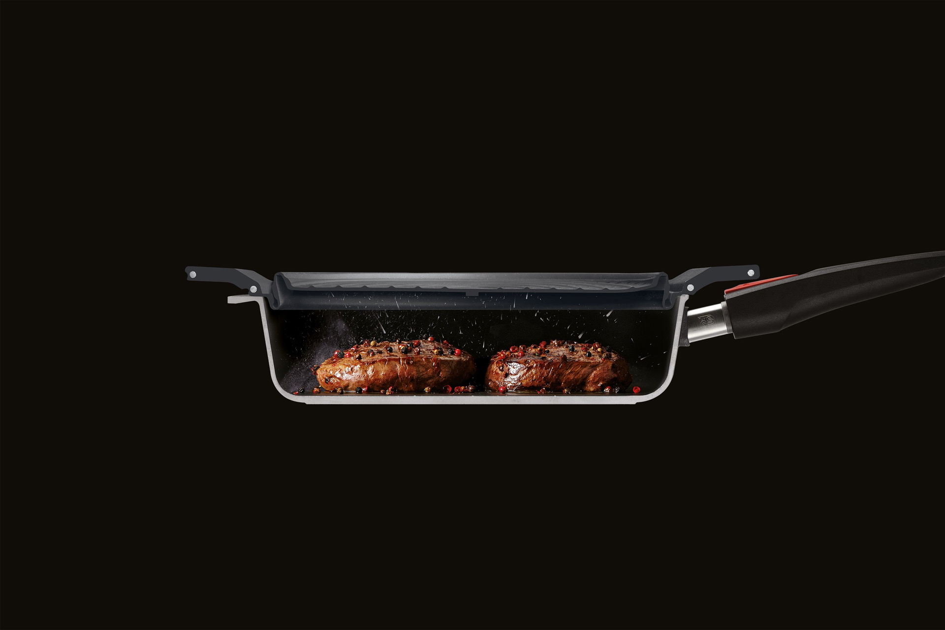 Im Querschnitt ist eine halbierte Pfanne zu sehen, in der zwei Stücke Fleisch angebraten werden. Der Steam it multifunktionale Silikoneinsatz dient als Spritzschutz.