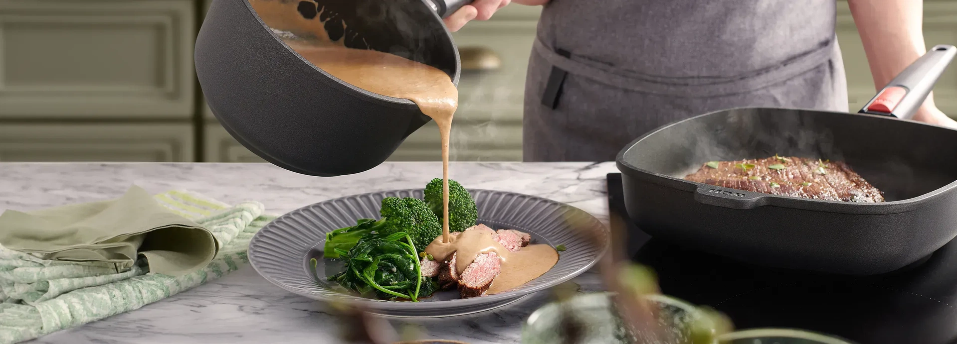 In der viereckigen Nowo Titanium Pfanne mit abnehmbarem Stiel wird das Fleisch scharf angebraten. Parallel dazu wird aus dem Nowo Titanium Stieltopf eine warme Sauce auf einen bereits portionierten Teller gegossen. Auf dem Teller liegen das dampfende Flei