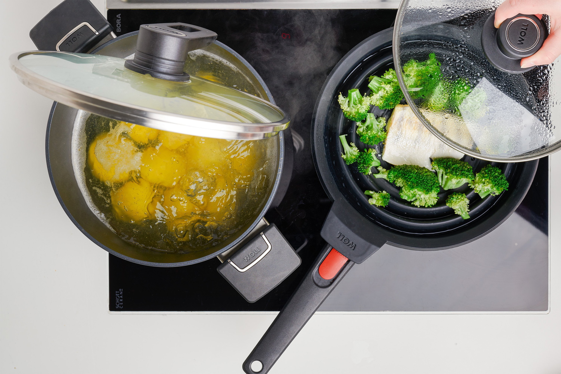 In einem runden Diamond Lite Topf werden Klöße gekocht. Der Smart Lid steht auf der Pfannenkante. In der Pfanne mit einem Silikoneinsatz wird Brokkoli und Fisch gedämpft.