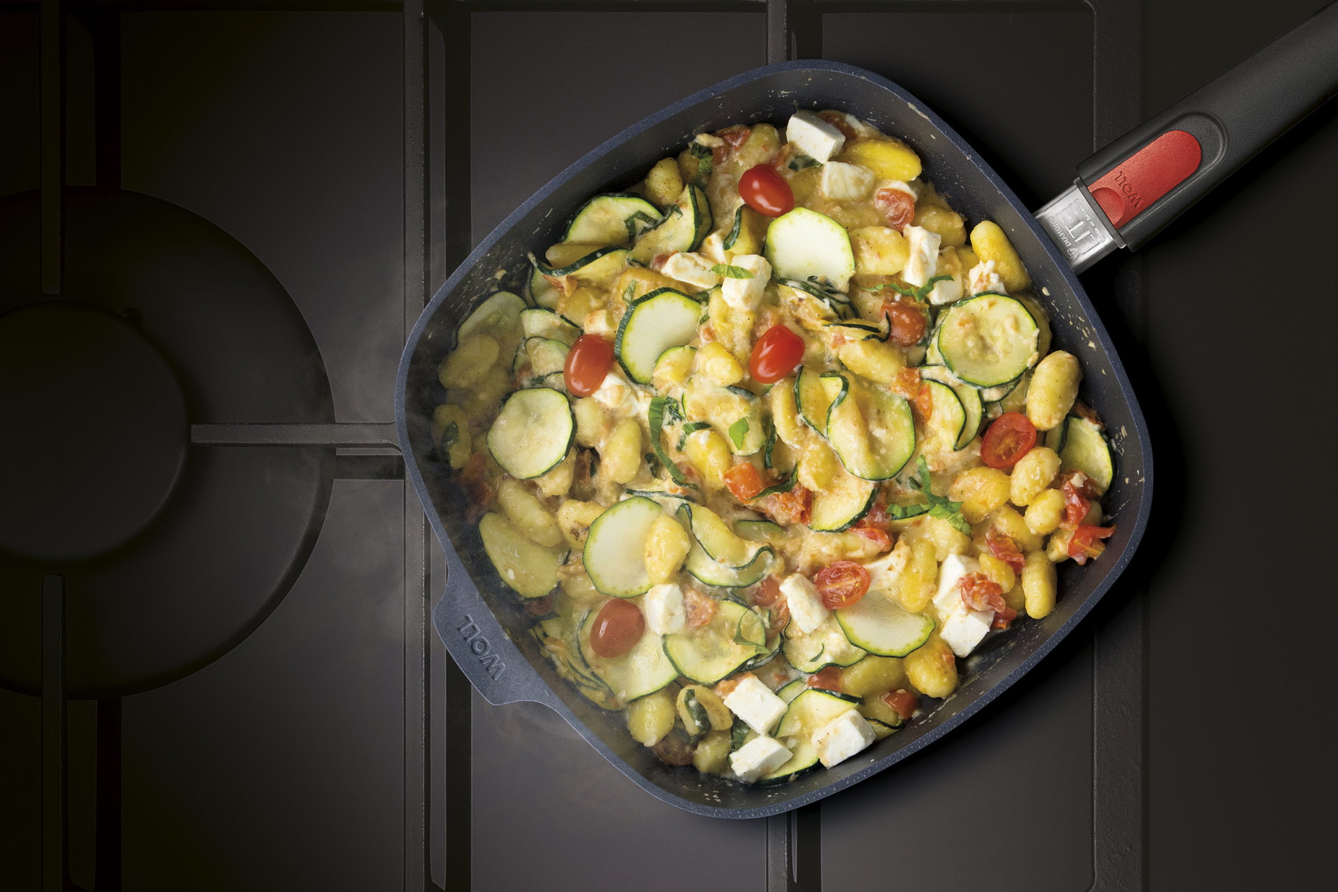 Auf dem Herd steht eine viereckige, heiße Diamond-Lite-Pfanne mit abnehmbarem Stiel. Darin befindet sich frisch zubereitete, dampfende Gnocchi mit Zucchini.