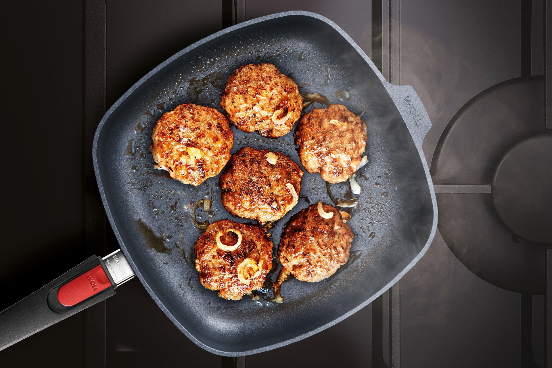 Auf dem Herd steht eine viereckige, heiße Diamond-Lite-Pfanne mit abnehmbarem Stiel ohne Deckel, in der Frikadellen angebraten werden.