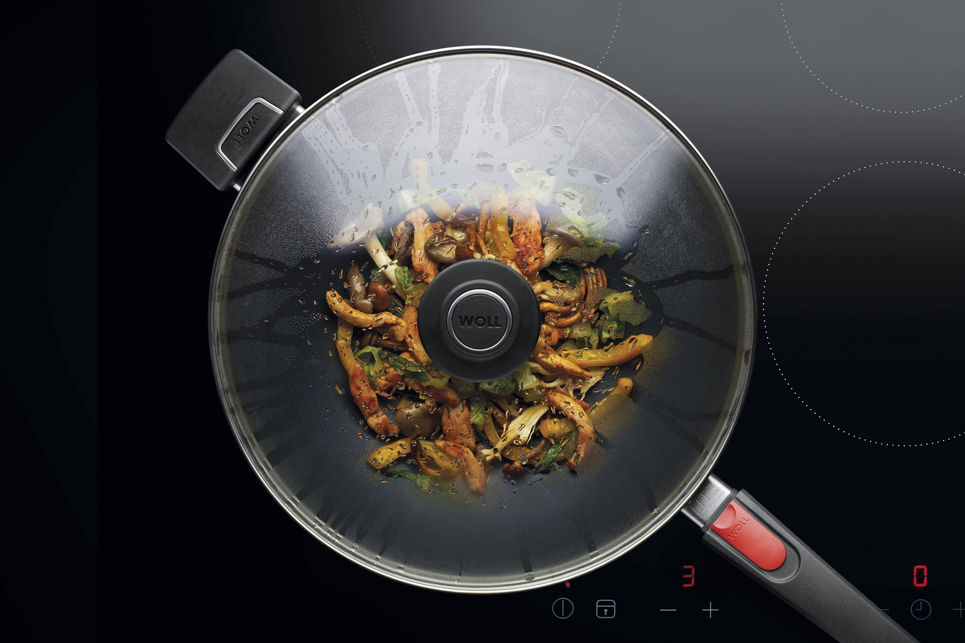 Auf dem Herd steht eine runde Diamond Lite Wok- und Rührpfanne  In dieser befindet sich ein  frisch zubereitetes Gericht. Am Glasdeckel hat sich Kondenswasser gebildet.