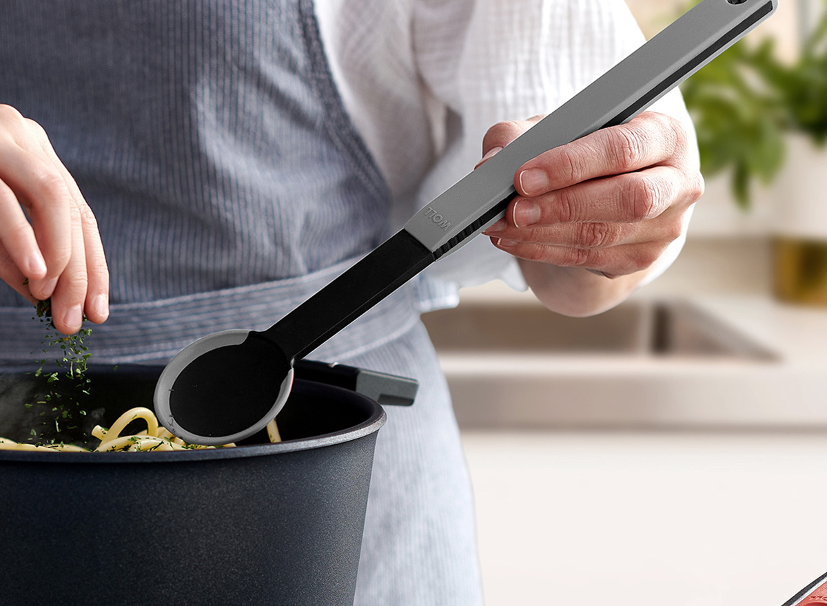 In einem Diamond Lite Topf werden frisch gekochte Nudeln mit einem grauen Kochlöffel der Serie Cock it umgerührt und mit Kräutern garniert.