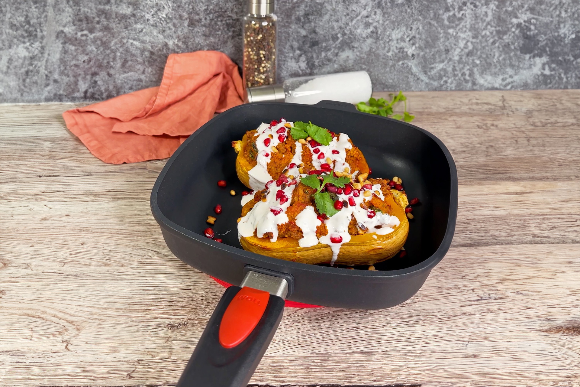 Auf einem Untersetzer auf dem Tisch steht eine Titan-Best-ViereckPfanne, in der sich zubereiteter Butternut-Kürbis mit Hackfleischfüllung befindet. Dahinter sind ein Stofftuch und Gewürze zu sehen.