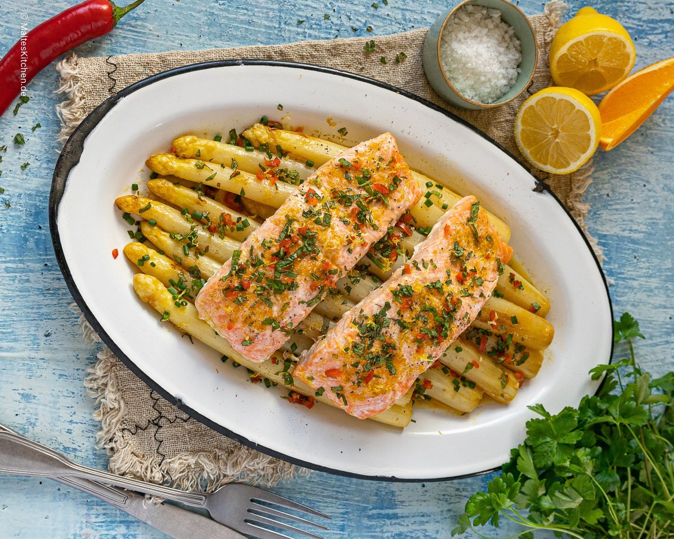 Auf einem Teller liegt frisch zubereiteter Ofenspargel mit Lachs und Orangen-Limetten-Butter.