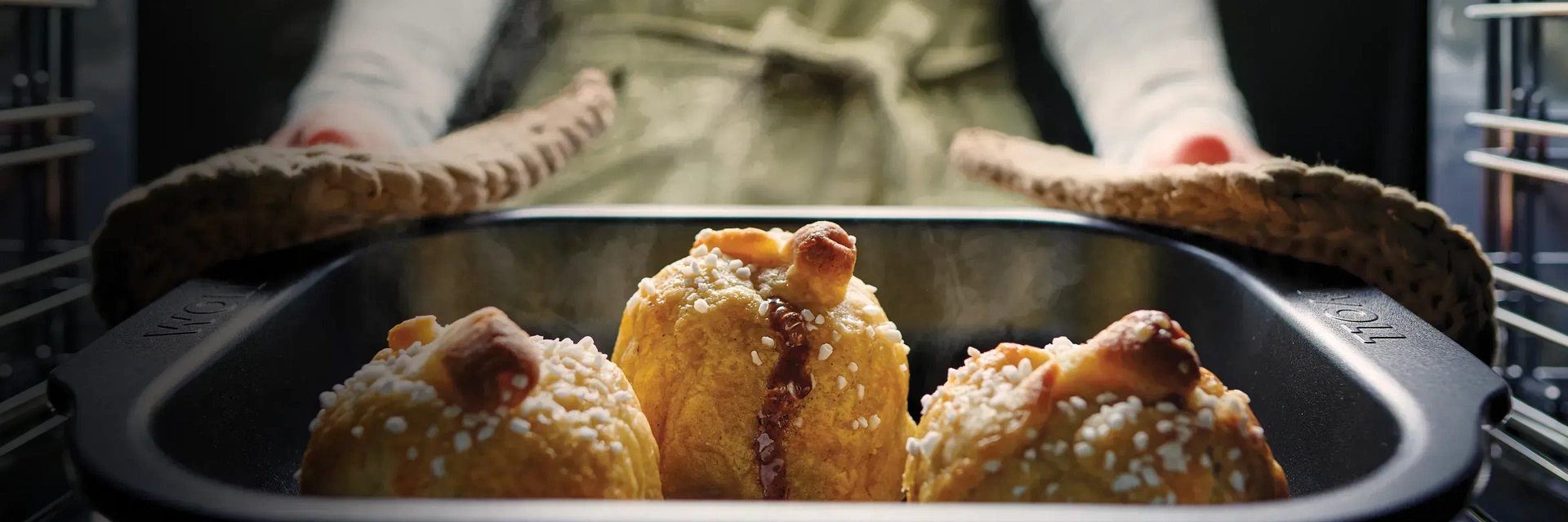 Eine heiße, viereckige Bratreine der Serie Roast it, beinhaltet ein dampfendes Gericht. Die Bratreine wird mit zwei Topflappen aus dem Backofen genommen.