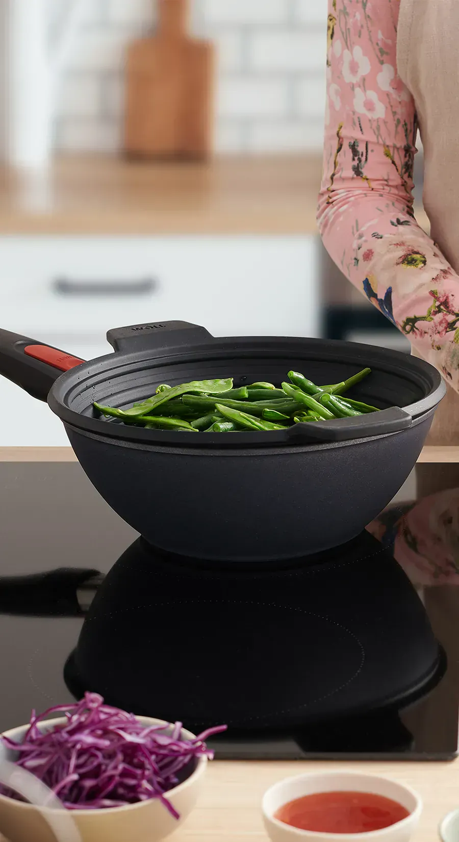 In dem runden Wok der Serie „Diamond Lite” wird mithilfe des Silikoneinsatzes „Steam it” Gemüse gedämpft. Daneben steht ein Teller mit frischem Essen, auf das etwas Limettensaft ausgepresst wird. Im Vordergrund sieht man zwei kleine Schüsseln, die jeweils