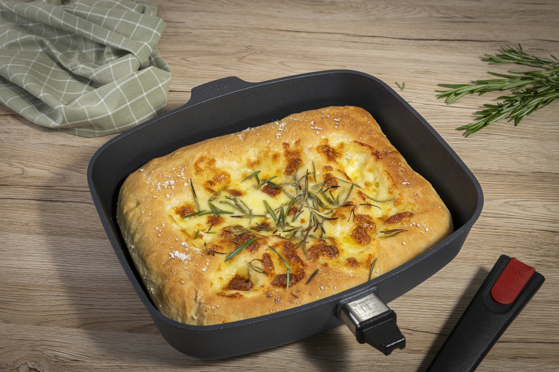 In einer heißen, viereckigen Diamond-Lite-Pfanne mit abgenommenem Stiel befindet sich frisch gebackenes Mozzarella-Brot. Darüber liegt ein Küchentuch.