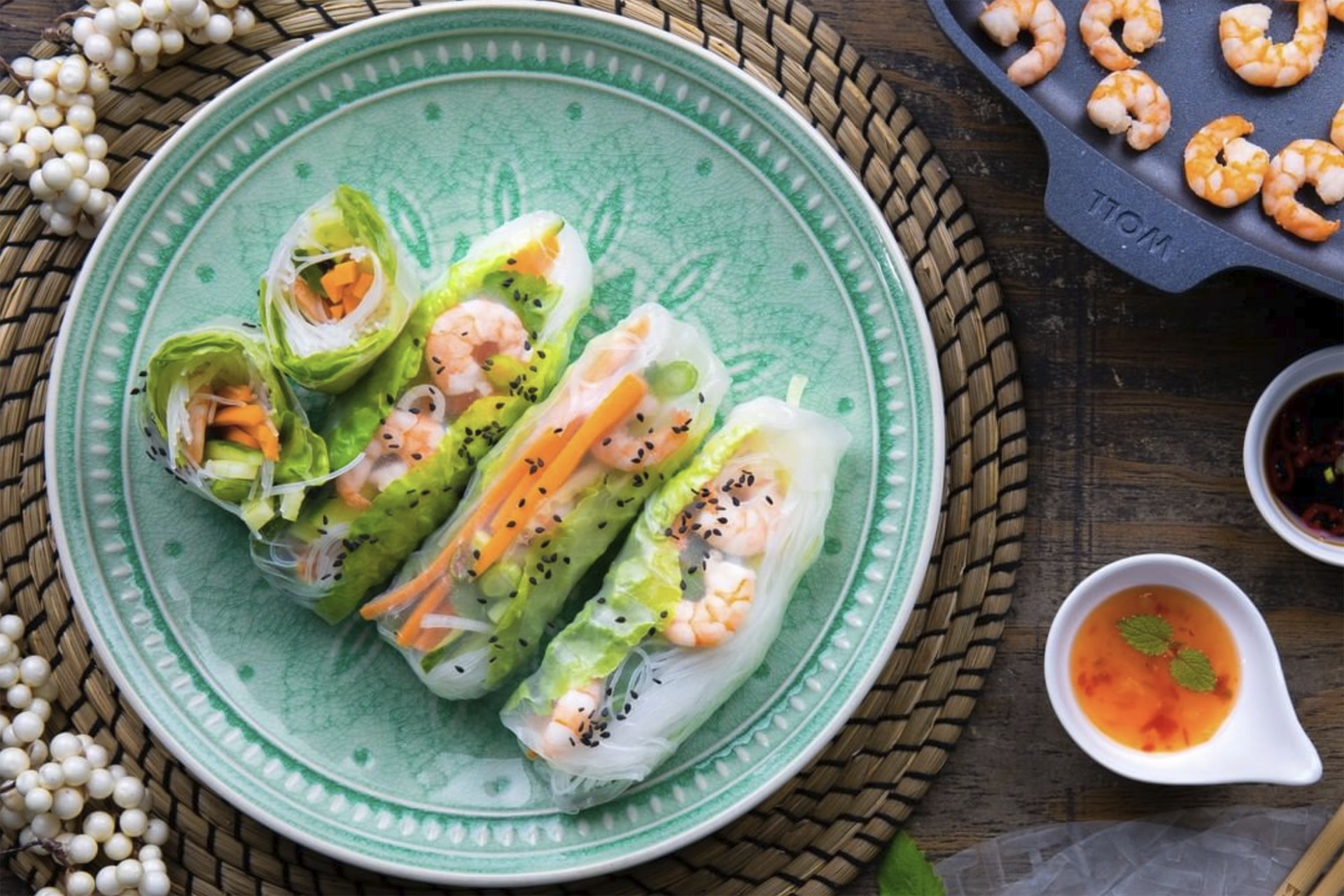 Auf einem Teller liegen gefüllte Sommerrollen. Rechts daneben stehen Dips. In einer viereckigen Pfanne aus der Serie Diamond Lite befinden sich weitere angebratene Garnelen.