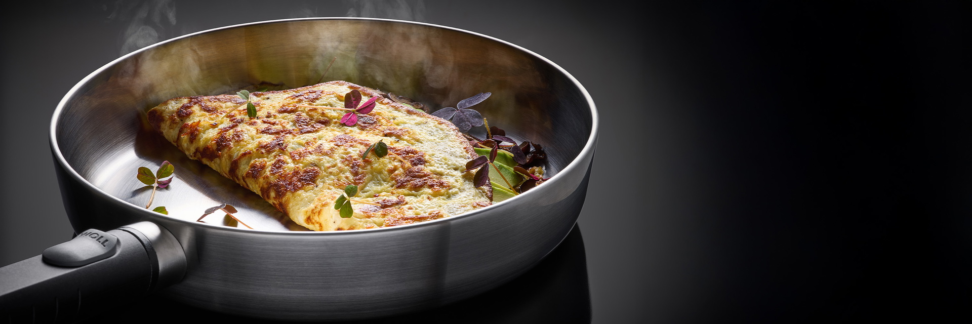 Eine runde, heiße Logic Steel Pfanne mit abnehmbaren Stiel beinhaltet ein dampfendes, gebackenes Omelette.