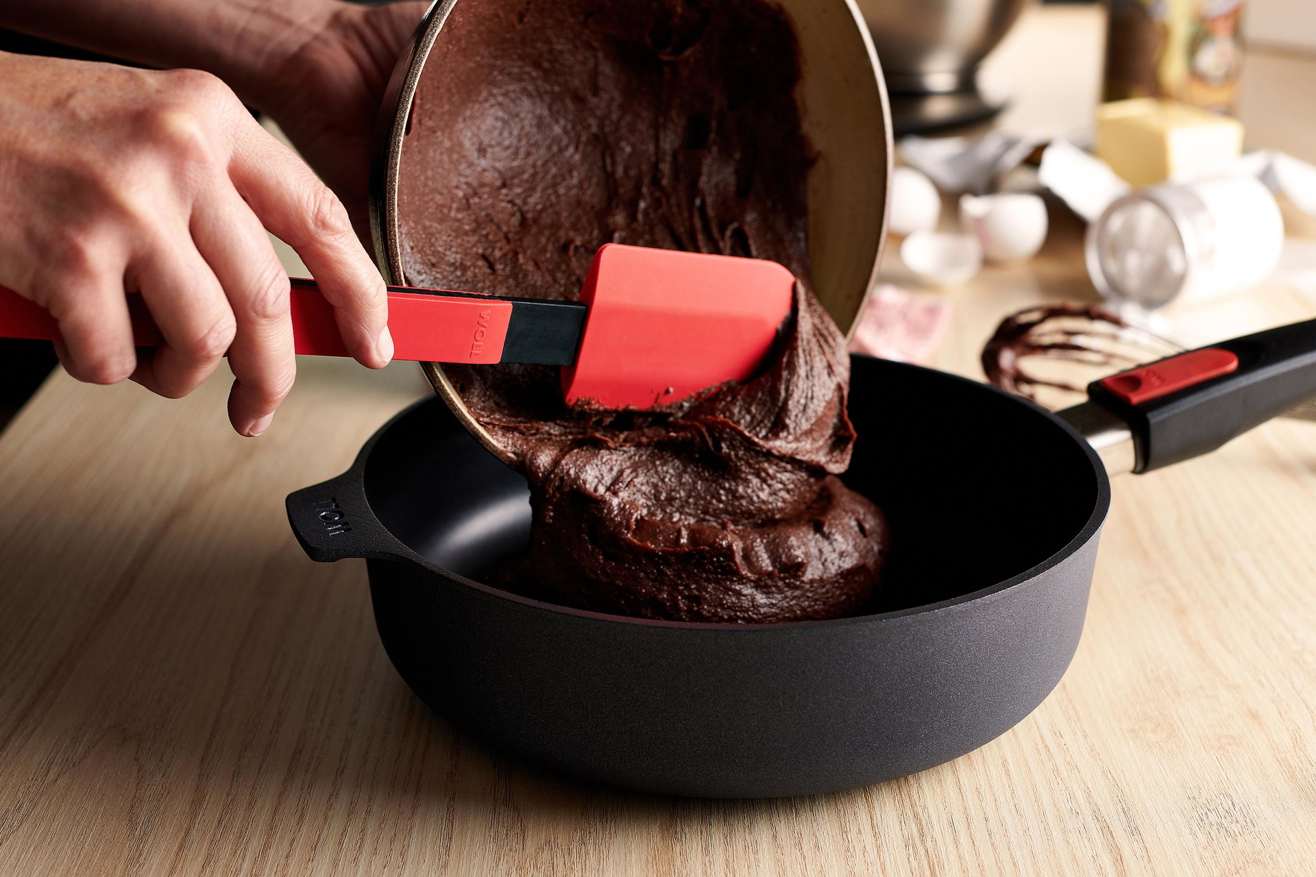 Der Kuchenteig wird mit einem roten Cook-it-Teigschaber aus der Schüssel direkt in die Diamond Lite Hochrandpfanne gegeben.
