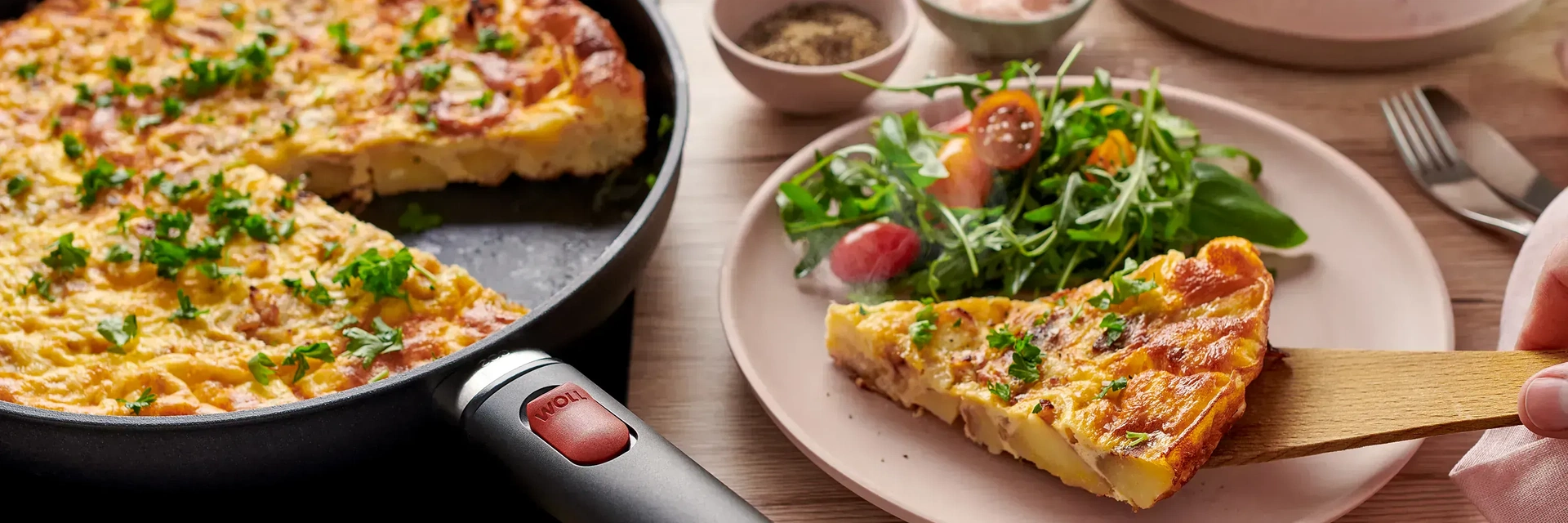 In einer runden Pfanne der Serie Eco Light QXR mit abnehmbarem Stiel befindet sich eine frisch zubereitete Spanische Tortilla. Ein Teil davon wird zusammen mit frischem Salat auf einem Teller serviert.