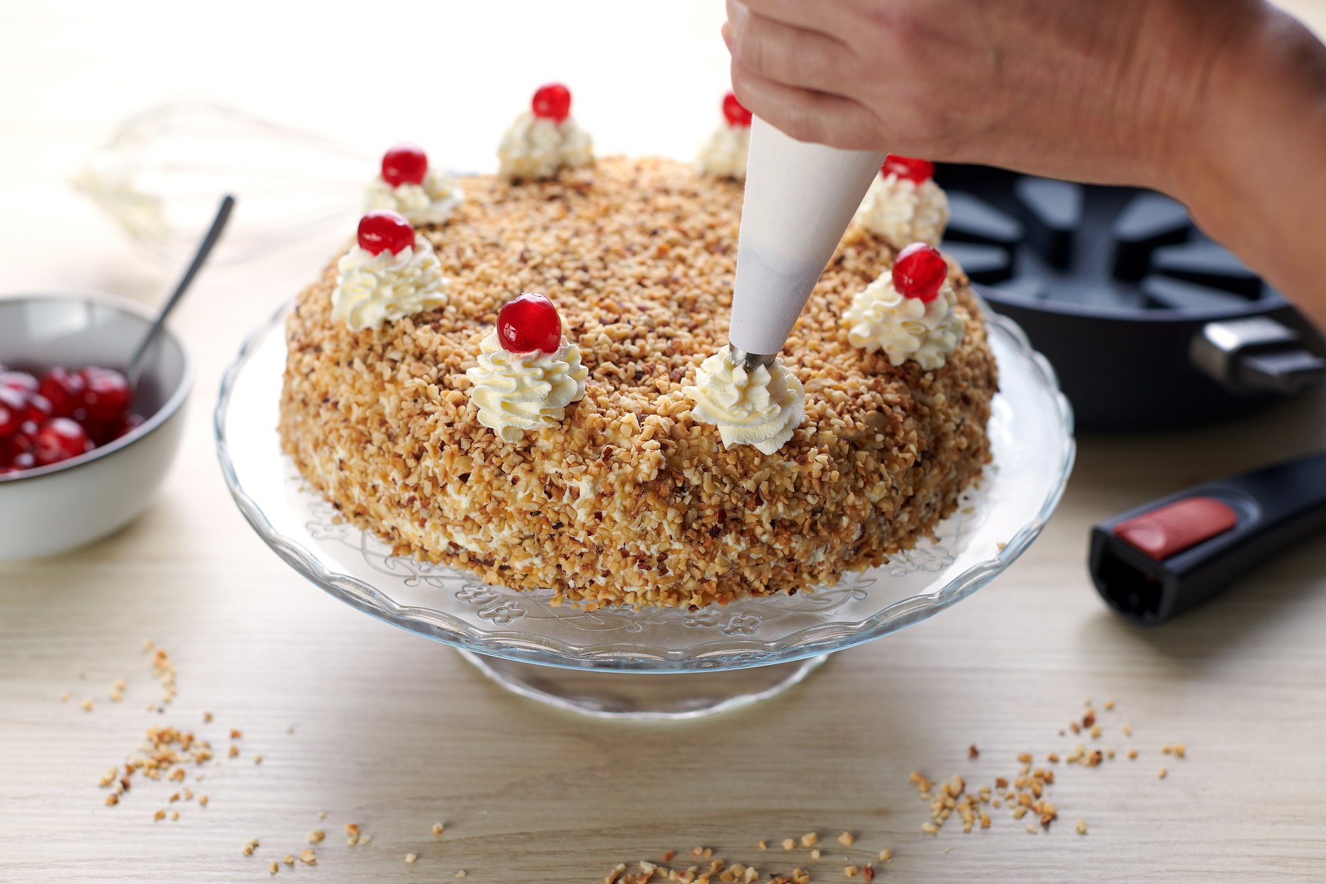 Auf einer Kuchenplatte steht ein Frankfurter Kranz mit Kirschfüllung. Der Kranz wird mit Sahnehauben und glasierten Kirschen verziert.