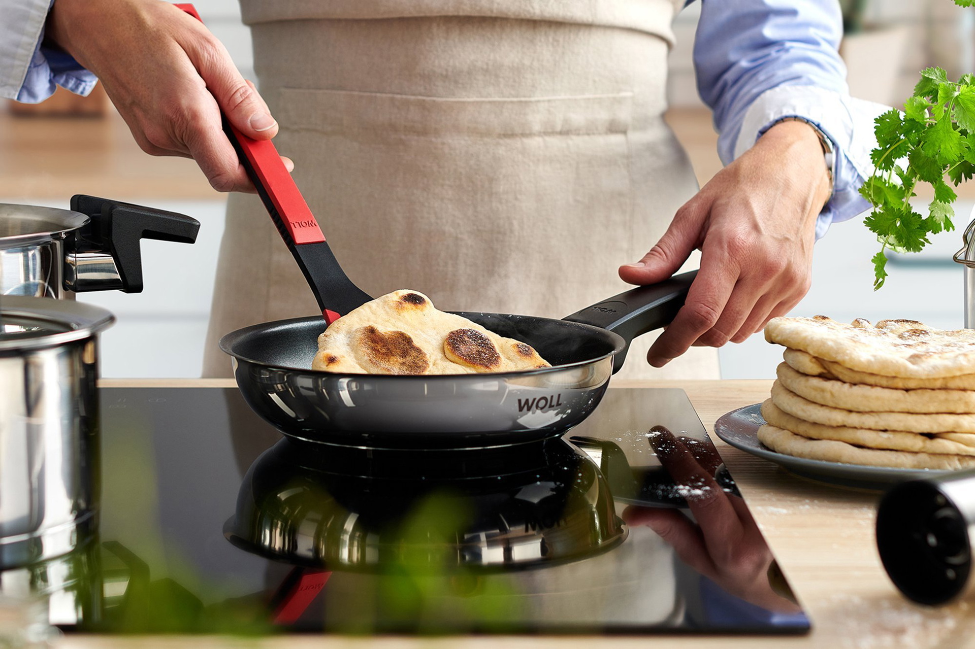 120NC_520NC_918NC_Mood_2000X1333_RGB In einer runden Concept Pfanne wird ein Fladenbrot mit eeinem Cock it gewendet. Daneben stehen zwei Concept Töpfe.