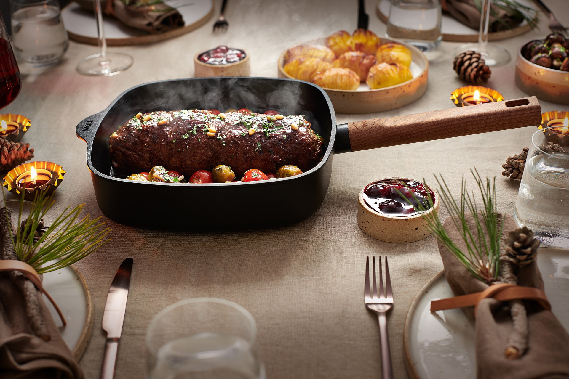 In einer viereckigen Logic-Pfanne mit festem Holzstiel befinden sich frisch zubereitete, gefüllte und gerollte Roastbeefs mit Hasselback-Kartoffeln, gebratenen Champignons, Rosenkohl und Kirschtomaten.