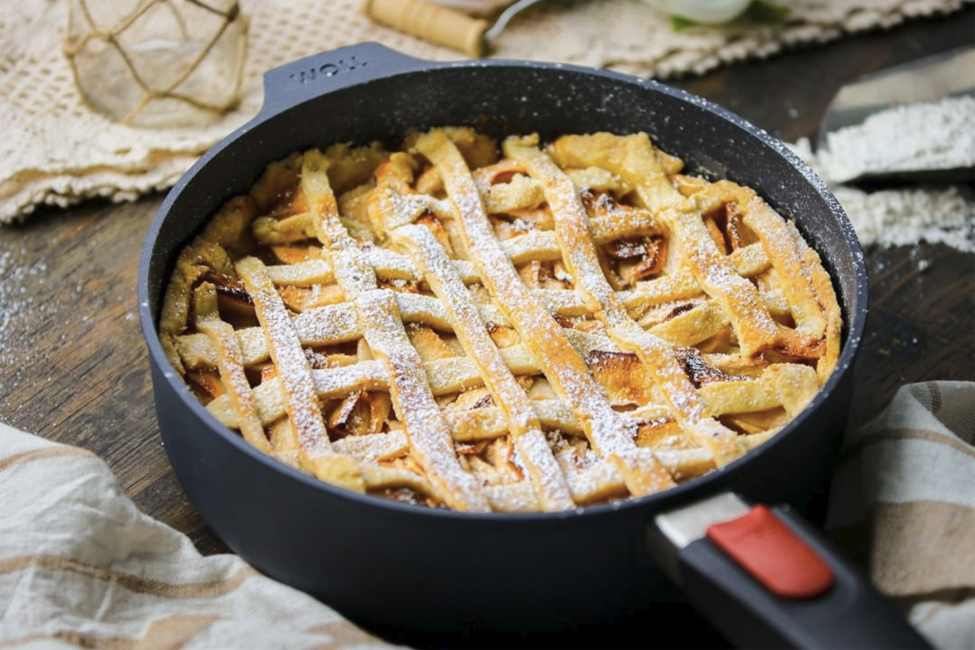 In einer runden Diamond-Lite-Pfanne mit abnehmbarem Stiel befindet sich ein frisch gebackener Apple Pie. Auf dem Tisch liegen außenrum Geschirrhandtücher und Zutaten.