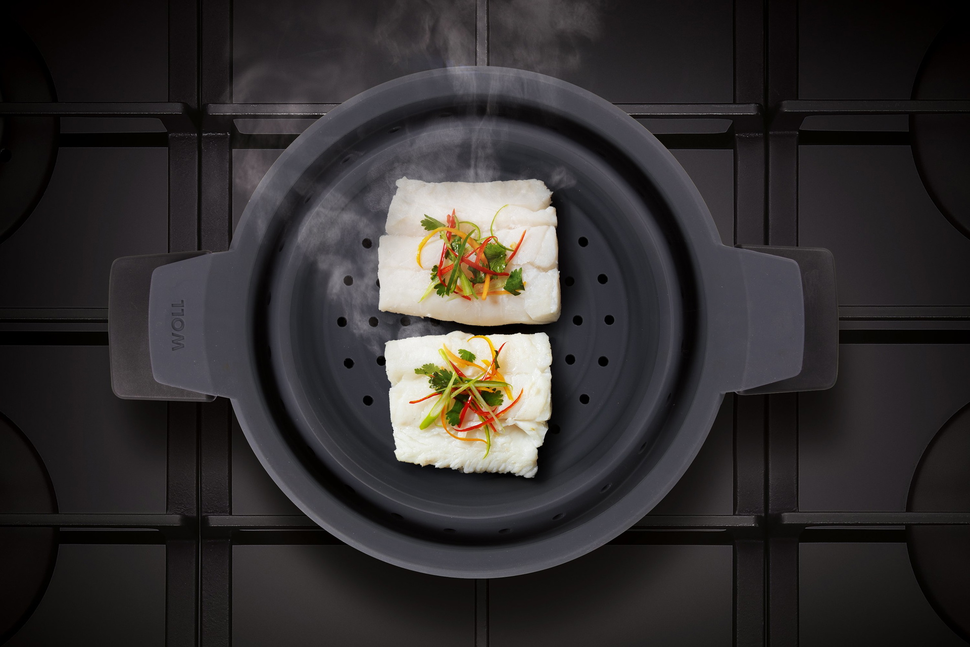 Auf dem Herd steht ein runder, heißer Diamond Active Lite Topf, in diesem befindet ein Steam it Multifunktionaler Silikoneinsatz. Im Silikoneinsatz wurde Kabeljau mit Antipastigemüse gedämpft.