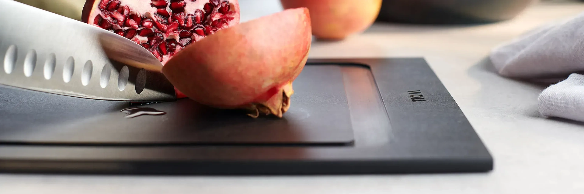 Ein Granatapfel wird auf einem Schneidebrett der Serie „Cut & Serve” mit einem Messer geteilt.