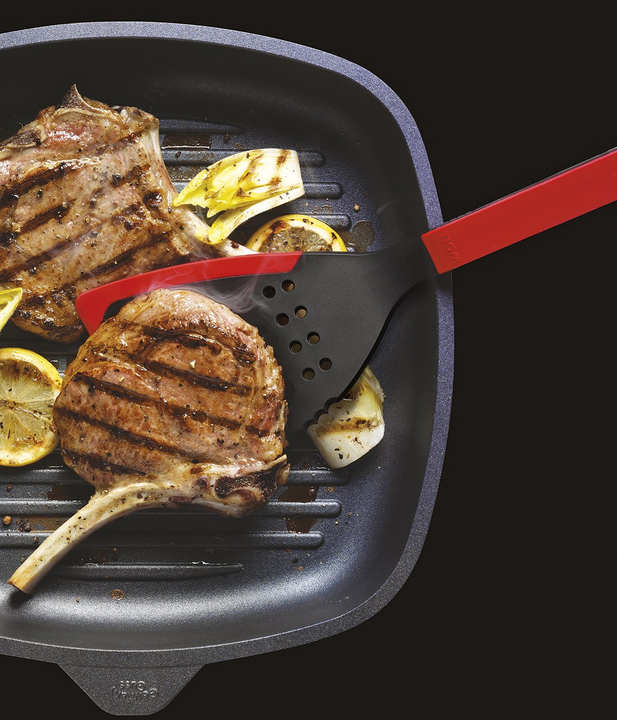 KU003_1200x1400_RGB In einer viereckigen Grillpfanne werden zwei Fleischstücke angebraten und mit einem roten Cock it Jumbo Pfannenwender gewendet.