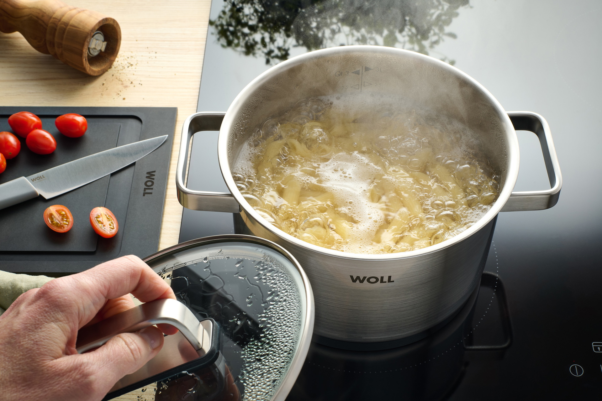 In einem runden Steel Topf ohne Glasdeckel werden Nudeln gekocht. Ein Messer liegt auf einem Schneidebrett.