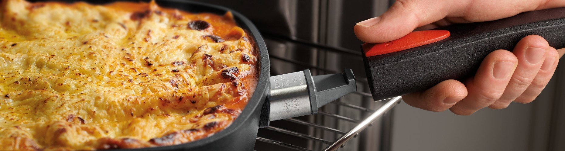 Auf dem Backofenrost steht eine viereckige, heiße Pfanne der Serie Titan Best, die ein überbackenes Gericht beinhaltet. Um die Pfanne aus dem Ofen zu holen, wird der Pfannenstiel wieder eingerastet.