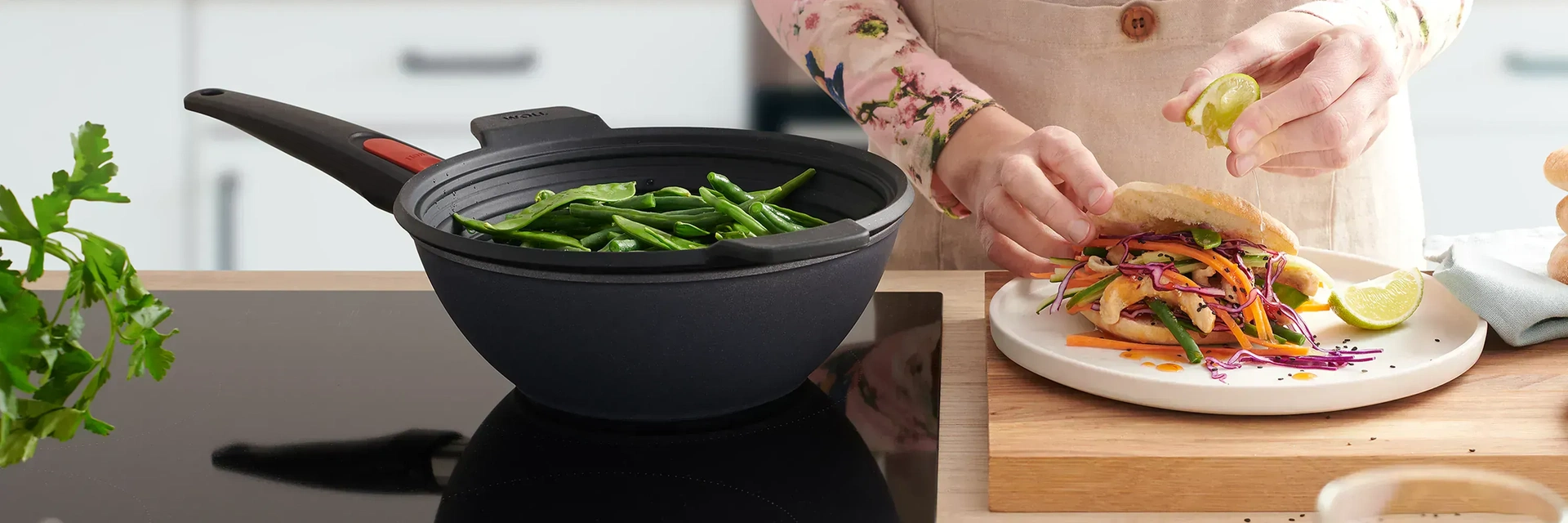 In dem runden Wok der Serie Diamond Lite mit abnehmbarem Stiel wird mithilfe des Silikoneinsatzes Steam it Gemüse gedämpft. Daneben steht ein Teller mit frischem Essen, auf das etwas Limettensaft ausgepresst wird.