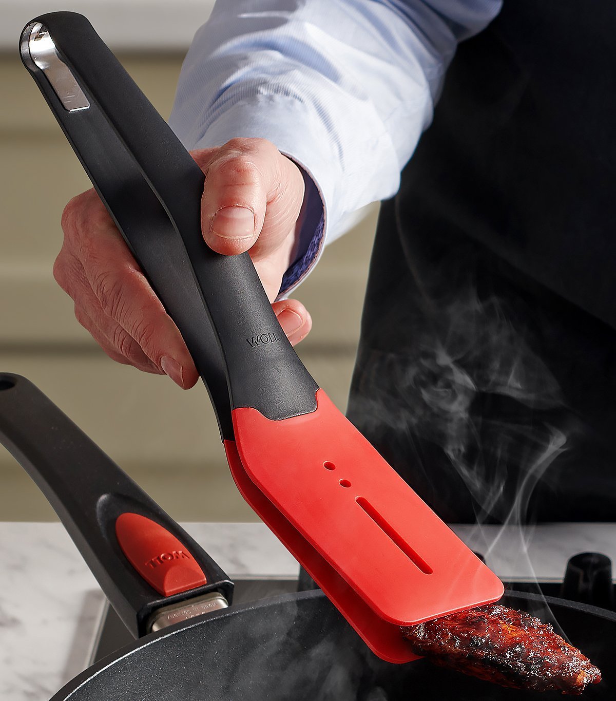 Ein dampfendes, angebratenes Stück Fleisch wird mithilfe der Cock it Küchenzange in der heißen Pfanne gewendet.