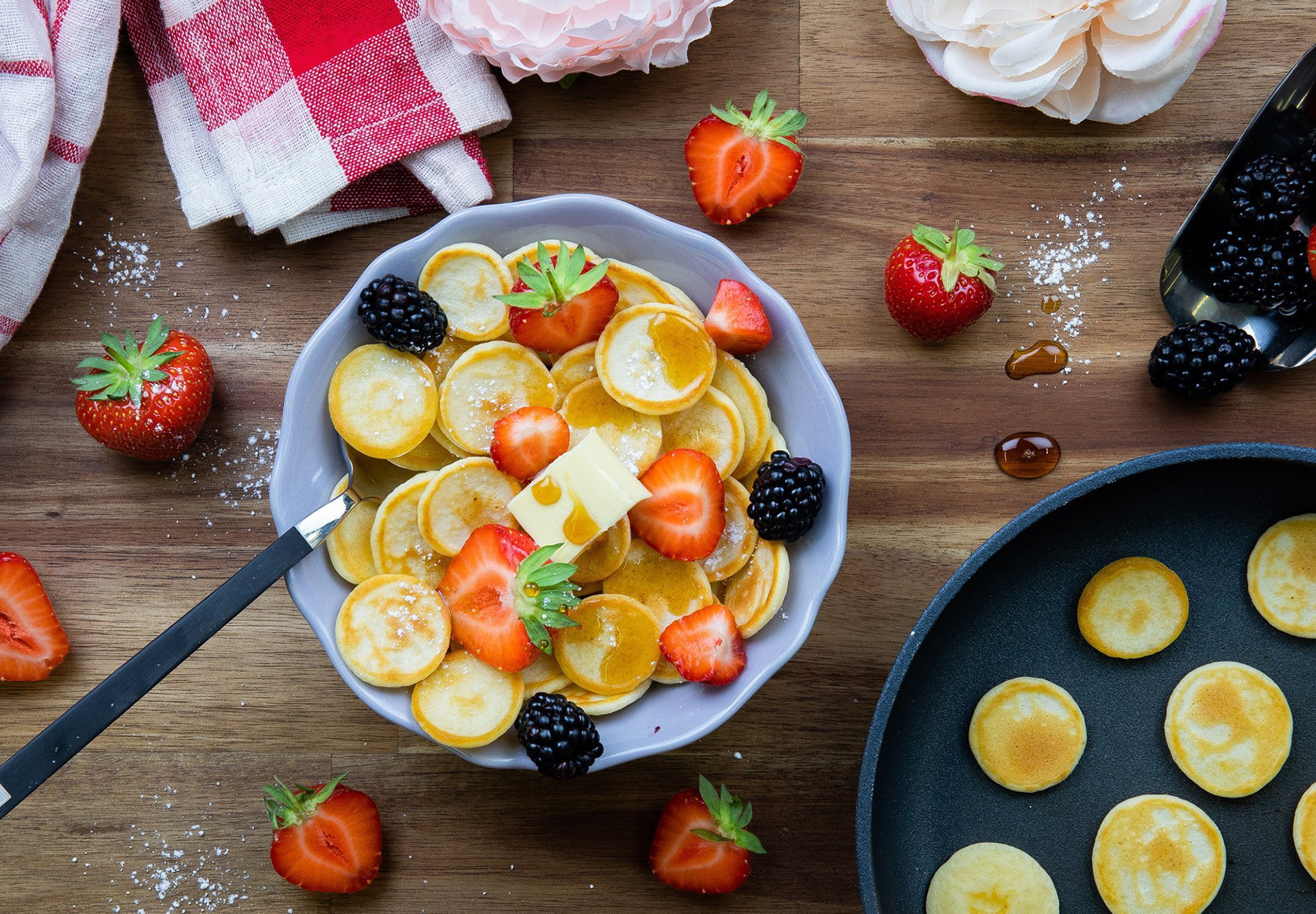 In einer Schüssel liegen mit Obst garnierte Mini-Pfannkuchen. Daneben steht die Diamond Lite Pfanne mit abnehmbarem Stiel, in der sie zubereitet wurden. Zusätzlich ist Obst außenrum als Dekoration platziert.