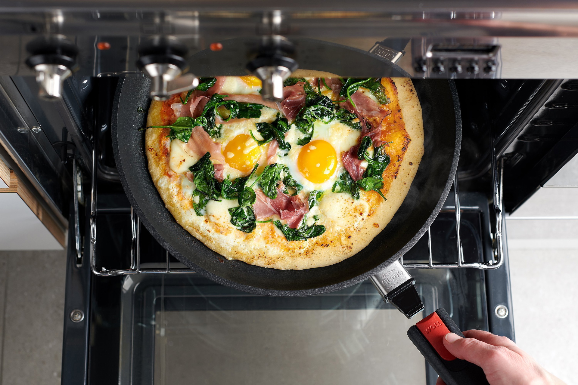 Auf dem Backofenrost steht eine runde, heiße Nowo-Pfanne mit frisch gebackener Pfannenpizza. Der abgenommene Stiel wird wieder eingerastet, damit die Pfanne aus dem Ofen genommen werden kann.