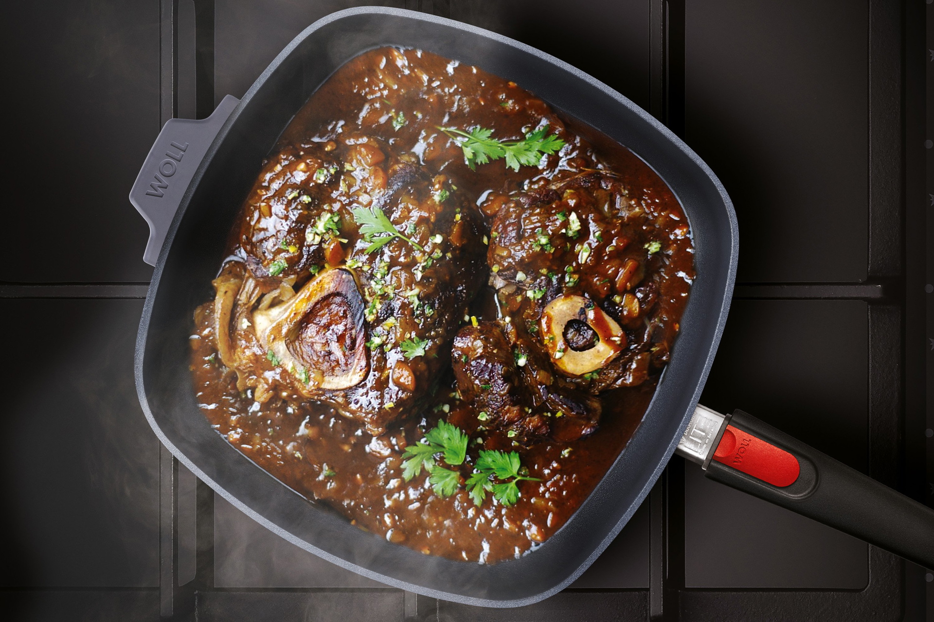 Auf dem Herd steht eine viereckige, heiße Diamond Lite Pfanne mit abnehmbarem Stiel und mit angebrachten Silikongriff befindet sich frisch zubereites dampfendes Ossobuco.