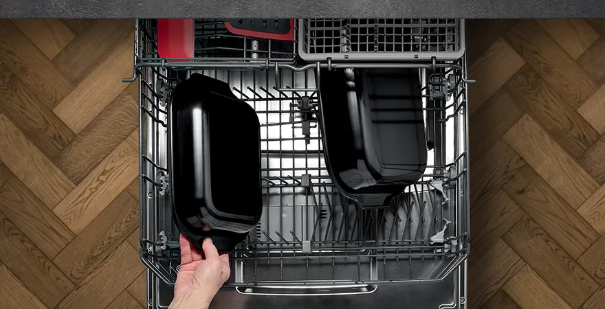 Die gereinigten Bratreinen der Serie Roast it! werden aus der Spülmaschine entnommen. Im oberen Fach liegen verschiedene Küchenhelfer der Serie Cook it!.
