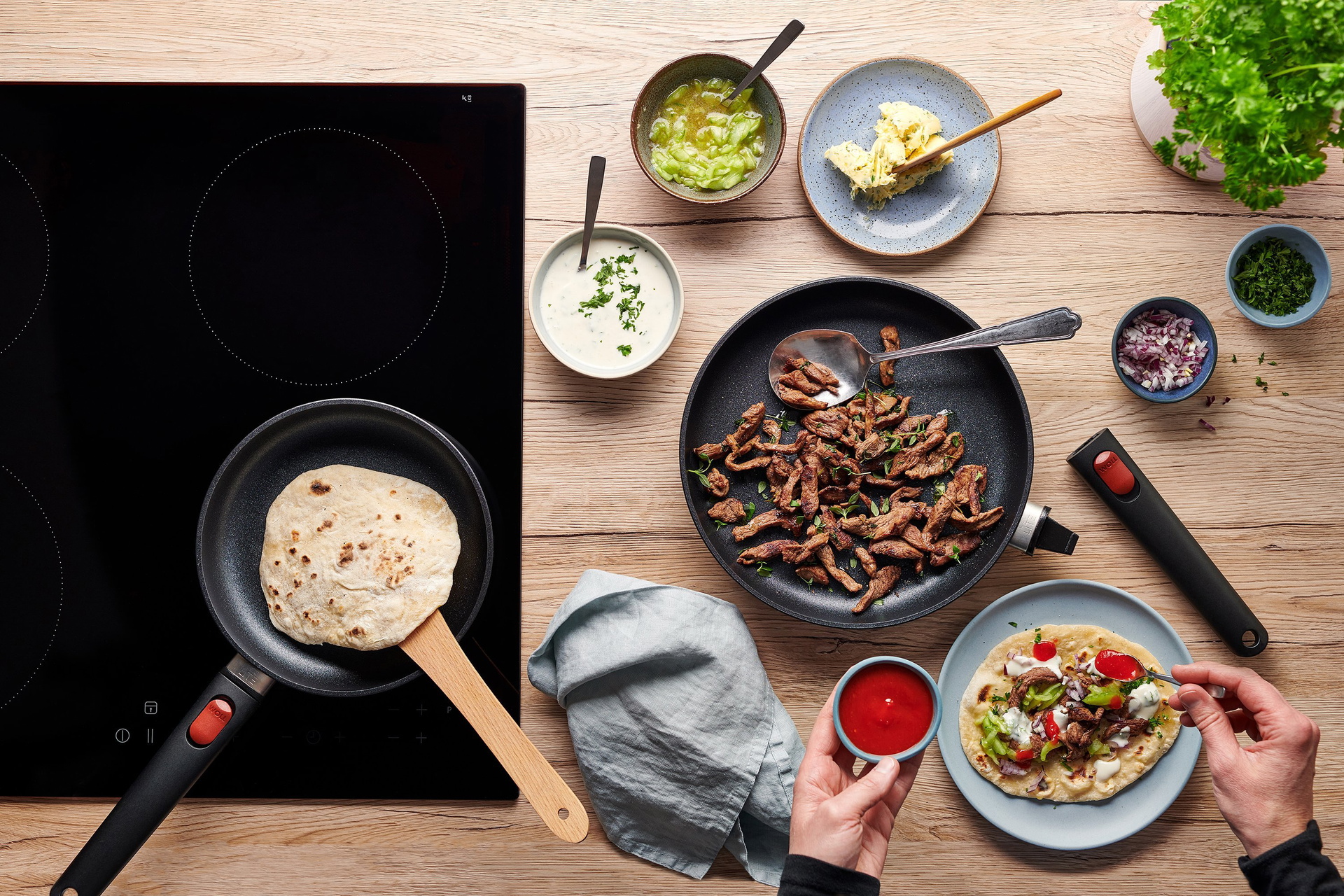 Auf dem Herd steht eine runde Pfanne der Serie „Eco Lite QXR” mit abgenommenem Stiel, in der frisches Fladenbrot gebacken wird. Auf der Arbeitsplatte steht eine größere, runde Pfanne derselben Serie mit abgenommenem Stiel, in der frisch angebratenes Lamm
