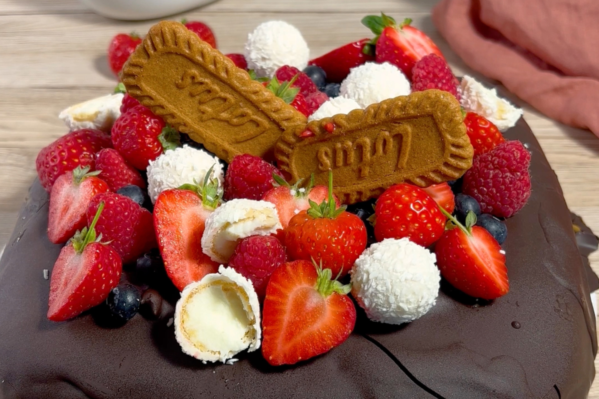 Eine Eistorte, dekoriert mit frischen Beeren, Raffaello und Lotus-Keksen.