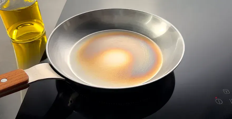 Auf dem Herd steht eine Carbon-Steel-Pfanne mit leichter Antihaftbeschichtung, daneben eine Flasche mit neutralem Öl.