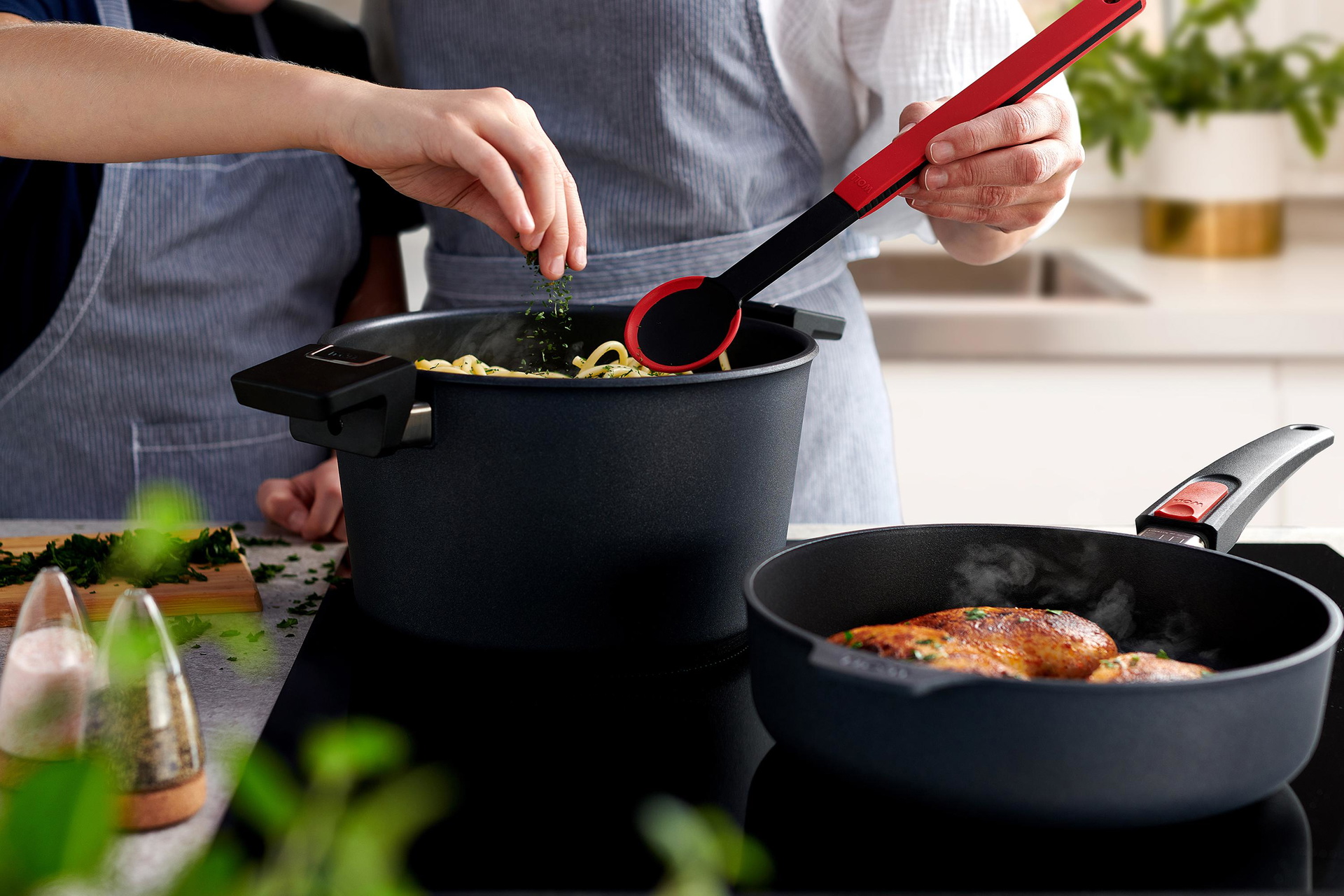 1724DPI_124DPI_1724DPS_124DPS_KU004_Mood In einem runden Diamond-Lite-Topf werden Nudeln mit einem Cock-it-Kochlöffel umgerührt. Daneben steht eine runde Pfanne, in der Fleisch angebraten wird.