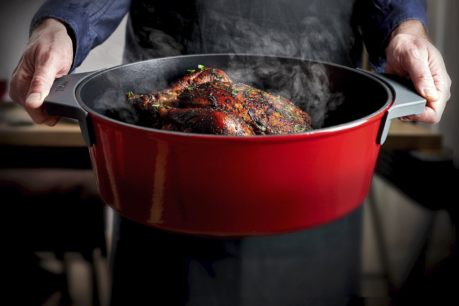 Der rote Iron Bräuter, in dem sich dampfendes Geflügel befindet, wird gehalten. Zum Schutz vor Hitze werden die Silikongriffe verwendet. 