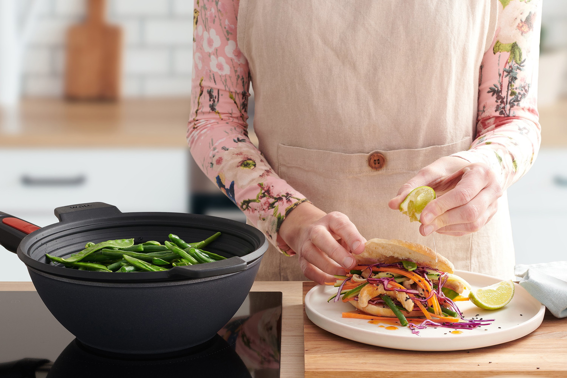 In dem runden Wok der Serie Diamond Lite mit abnehmbarem Stiel wird mithilfe des Silikoneinsatzes Steam it Gemüse gedämpft. Daneben steht ein Teller mit einem gefüllten Fladenbrot, auf das etwas Limettensaft ausgepresst wird.