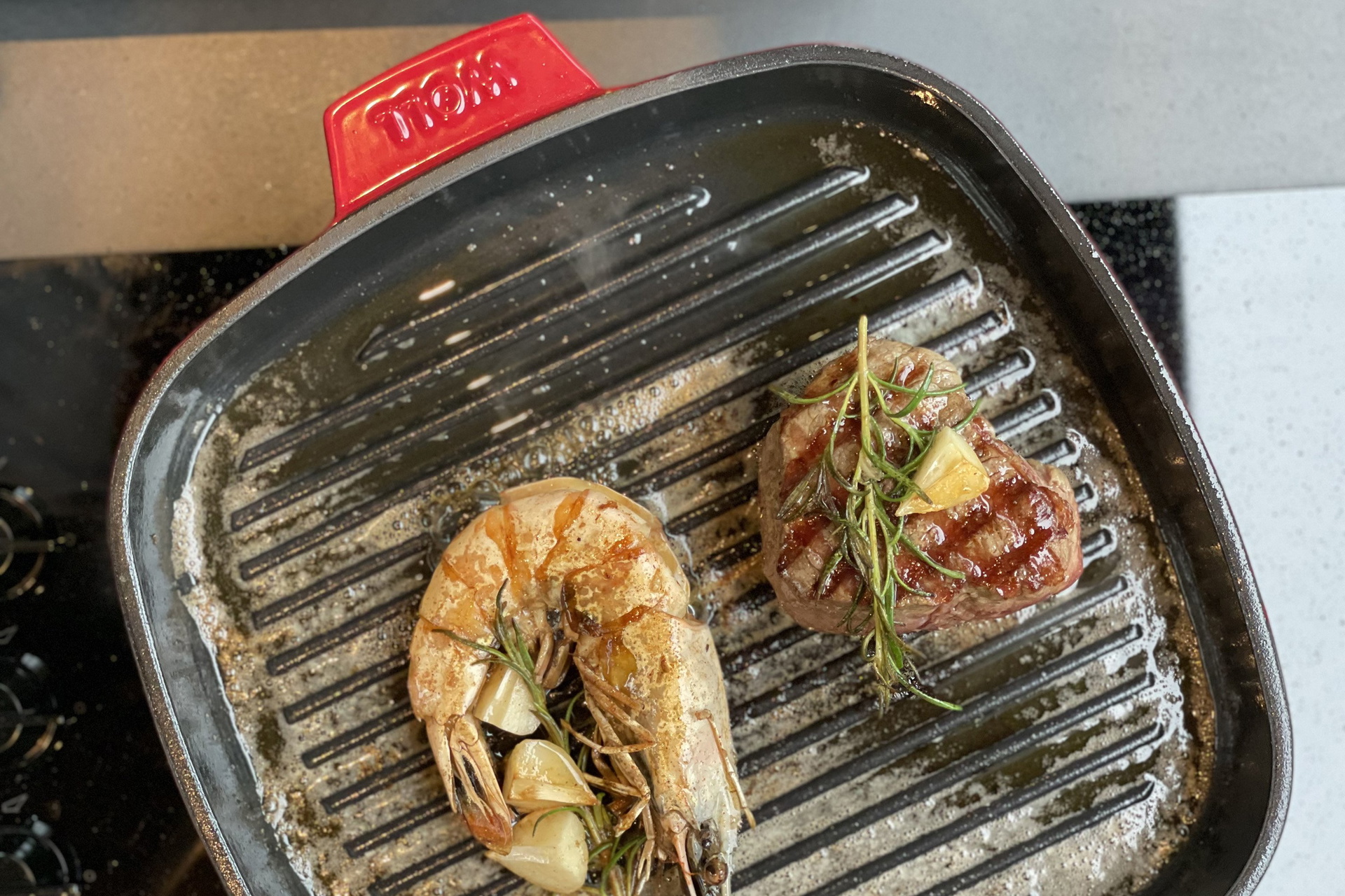 In einer heißen, viereckigen Grillpfanne der Serie „Iron“ wird eine Garnele und ein Stück Fleisch angebraten.