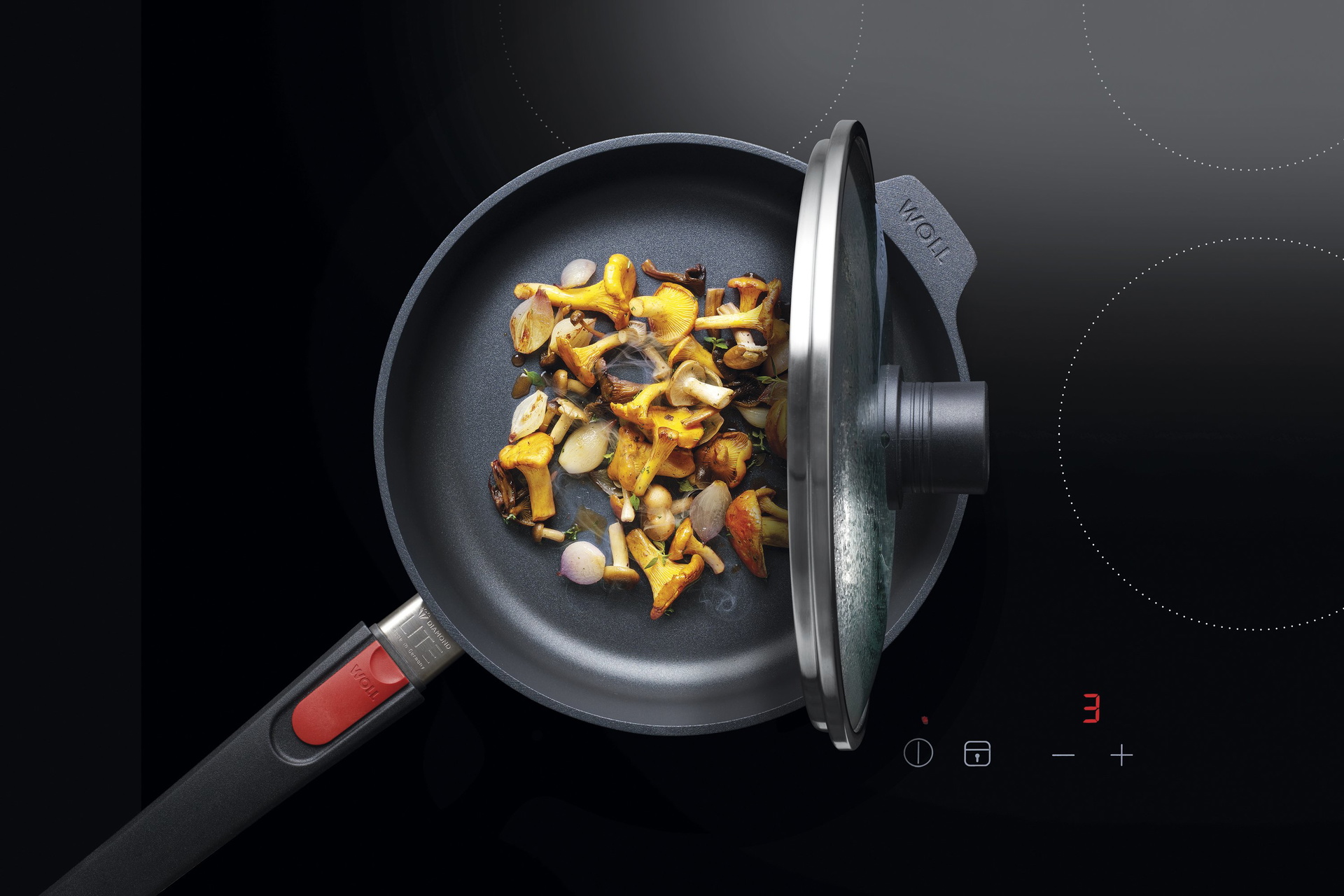 Auf dem Herd steht eine runde Diamond-Lite-Pfanne, in der ein Gericht zubereitet wird. Der Smart Lid steht auf der Pfannenkante.