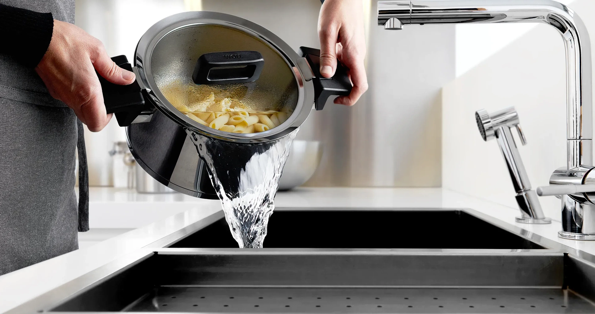 Das Nudelwasser wird aus dem Edelstahltopf der Serie Concept in die Spüle gegossen. Durch die angehobene Position des Glasdeckels ist ein sicheres Abgießen möglich.