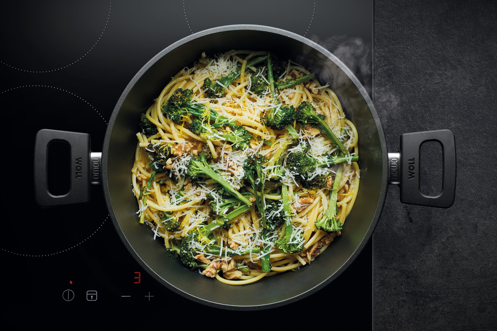 Auf dem Herd steht eine runde, heiße Kasserolle Topf der Serie Nowo. Darin befindet sich frisch zubereitete Spaghetti mit Brokkoli, Walnüssen und Parmigiano Reggiano.