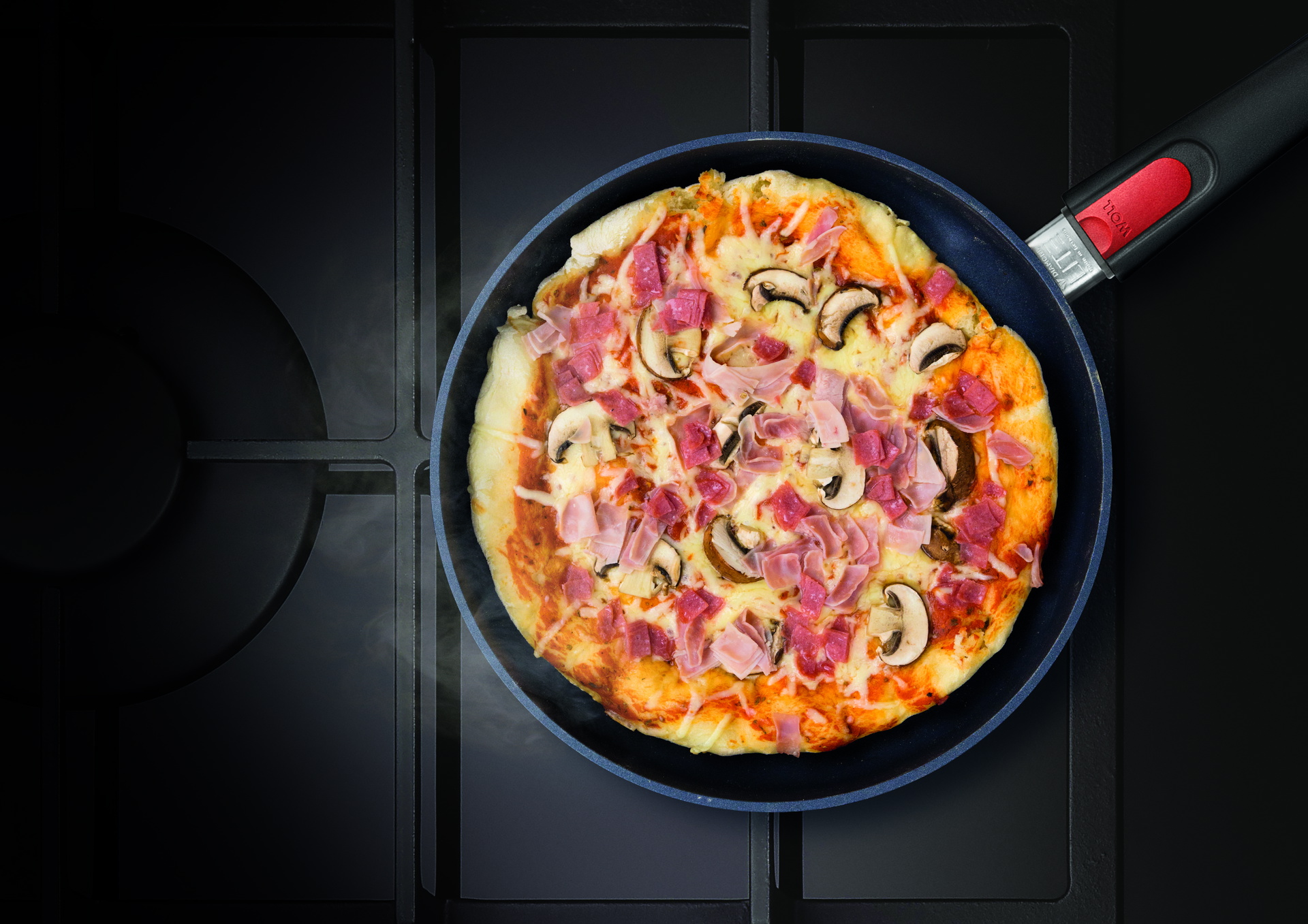 Auf dem Herd steht eine runde, heiße Diamond-Lite-Pfanne mit abnehmbarem Stiel, in der sich frisch zubereitete, dampfende klassische Pizza befindet.