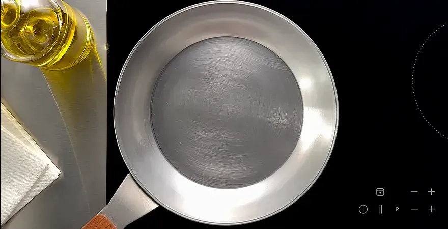 Auf dem Herd steht neue eine Carbon-Steel-Pfanne. Daneben stehen eine Flasche mit neutralem Öl und darunter liegt ein Stück Küchenrolle bereit.
