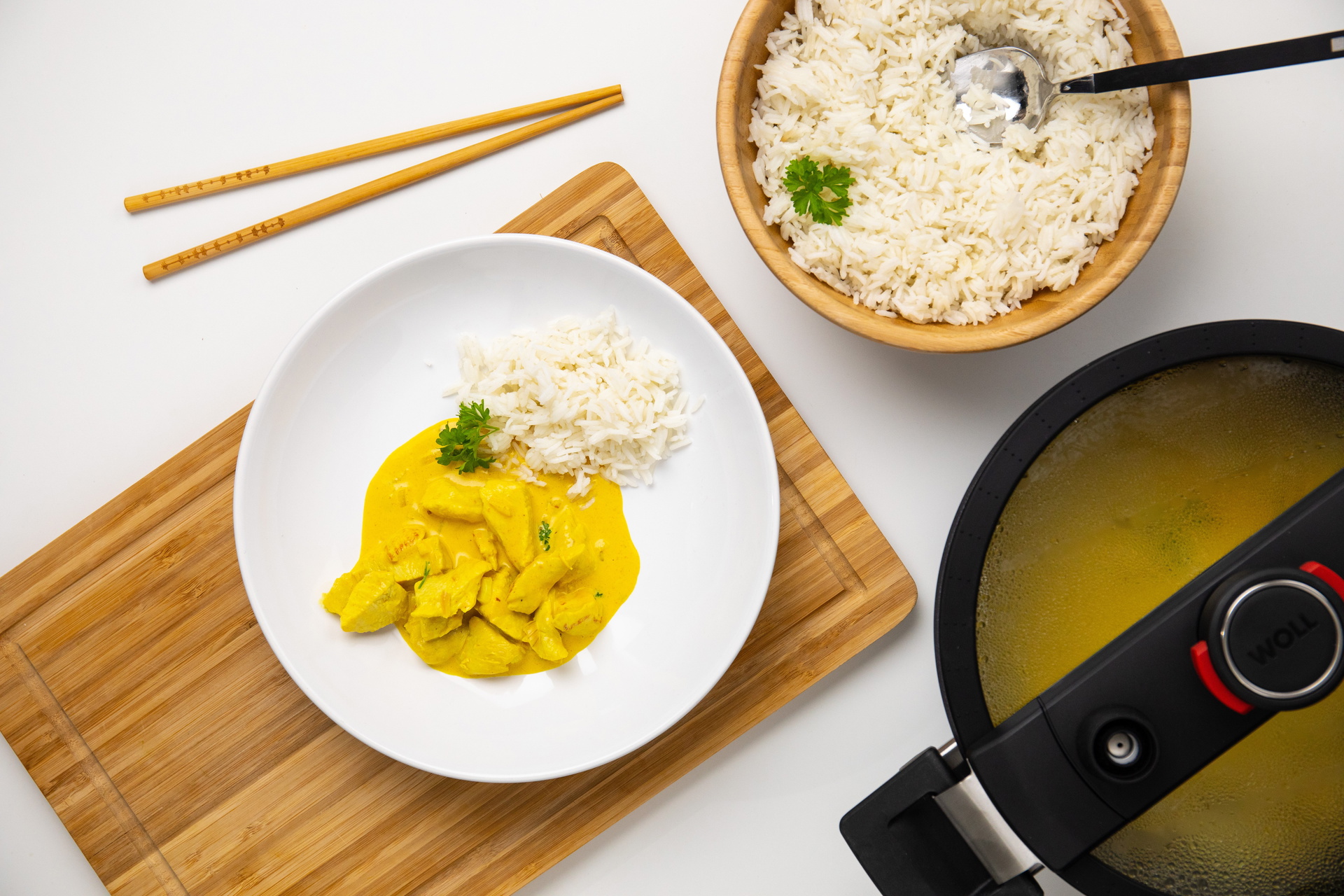 In einem heißen, runden Niederdrucktopf „Diamond Active Lite“ mit Deckel befindet sich indisches Butter Chicken. Daneben steht eine Schüssel mit Reis, auf einem Teller wird das Gericht mit Reis angerichtet.