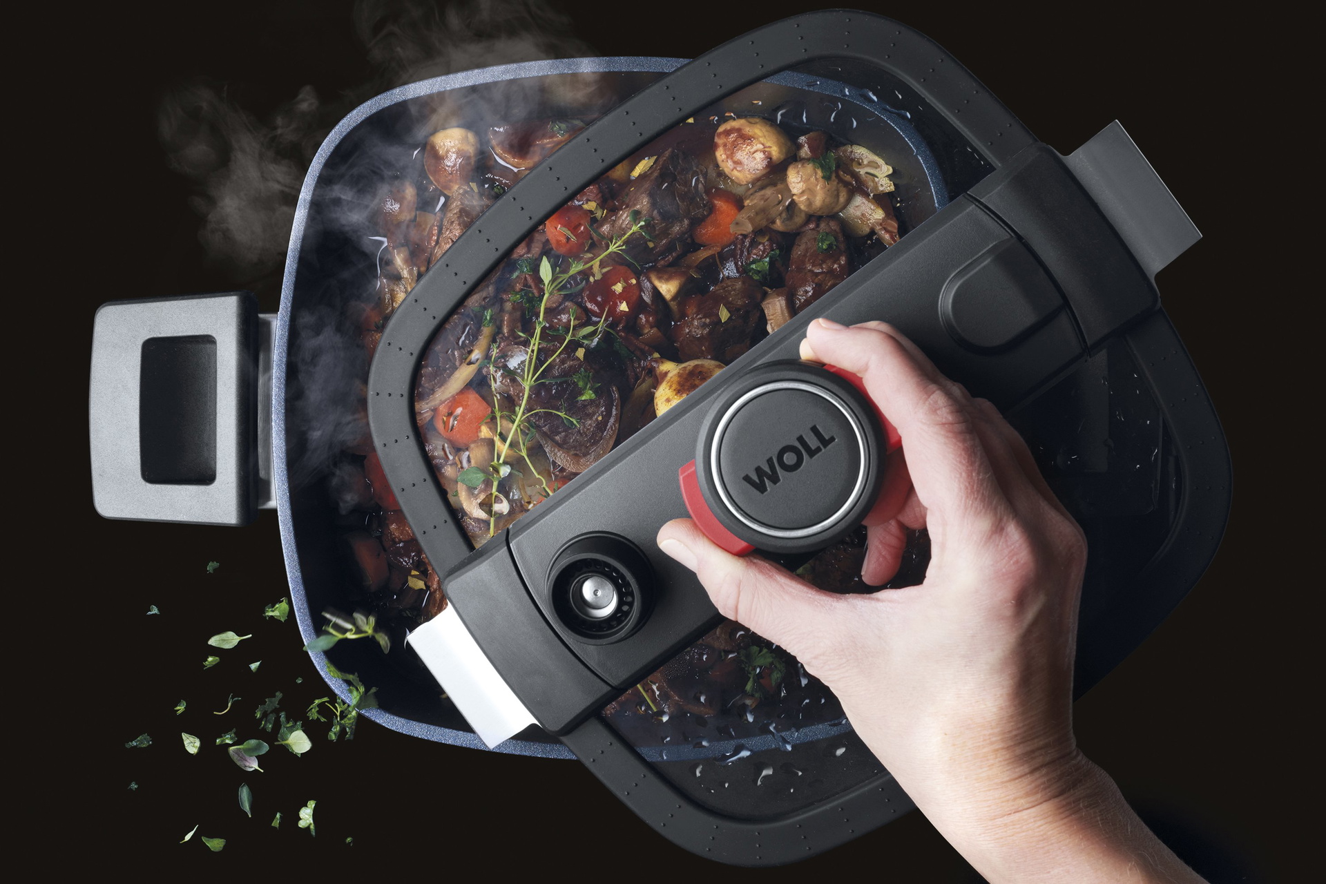 In einem heißen, viereckigen Niederdrucktopf der Serie „Diamond Active Lite” wird ein dampfendes Gericht zubereitet. Der Glasdeckel wurde mit einer Hand angehoben.