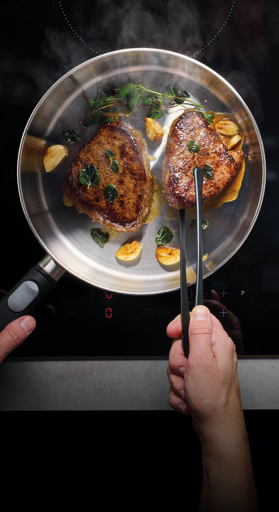 In einer heißen, runden Logic-Steel-Pfanne werden zwei Fleischstücke angebraten.